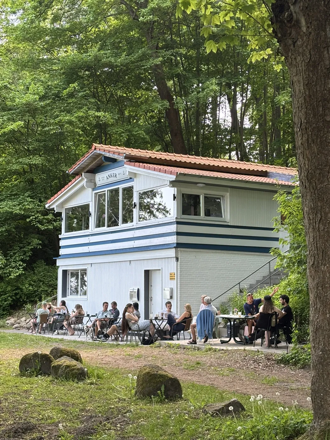 Das Anker No°4 von außen, Gäste sitzen auf der Terrasse unter den Bäumen